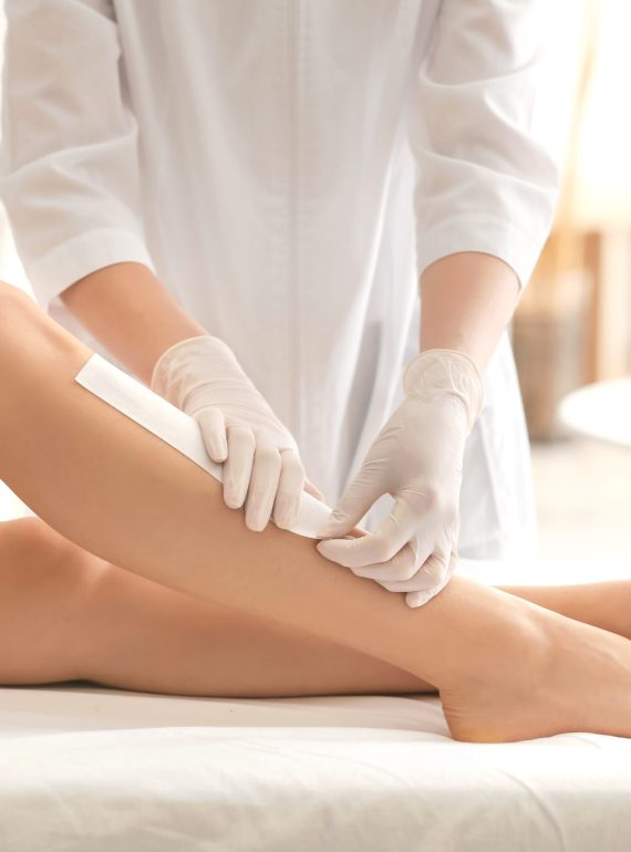 Beautician waxing female legs in spa center