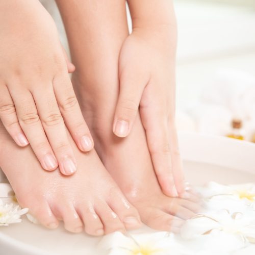 closeup view of woman soaking her hand and feet in dish with water and flowers on wooden floor. Spa treatment and product for female feet and hand spa. white flowers in ceramic bowl.